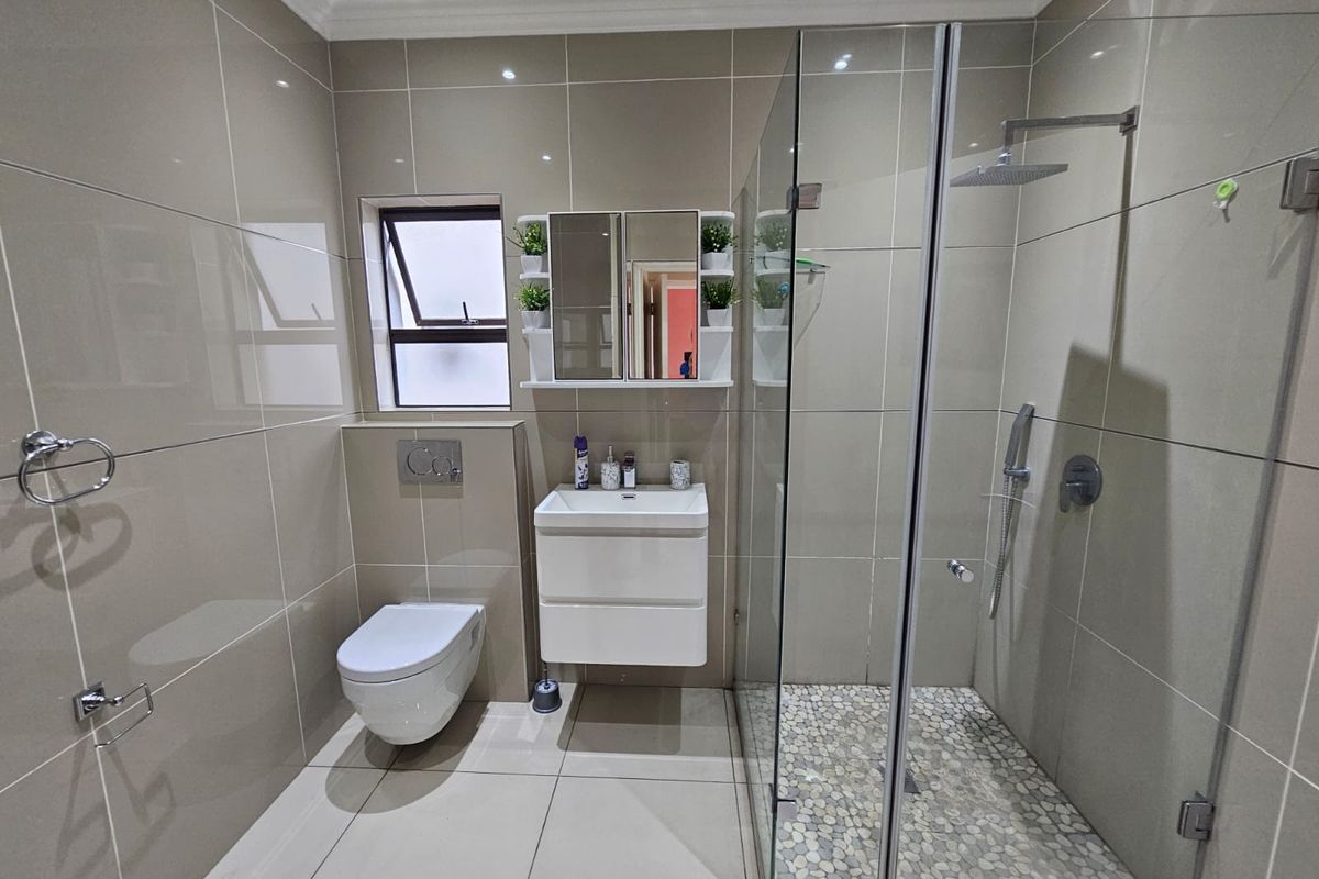 Modern bathroom featuring a frameless glass walk-in shower with pebble flooring, wall-mounted toilet, and a sleek vanity unit with integrated mirror cabinet.