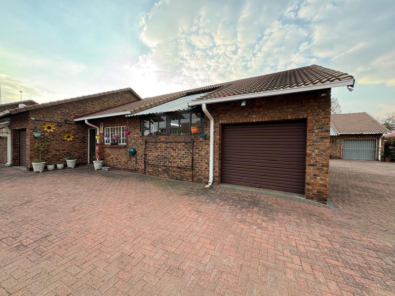 Exterior view of a face brick townhouse featuring a paved driveway, tiled roof, and a secure roller garage door.