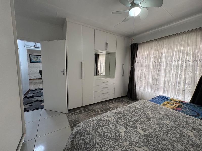 A well-maintained bedroom featuring built-in cupboards with integrated vanity, tiled flooring, and a ceiling fan, offering a clean and functional living space.