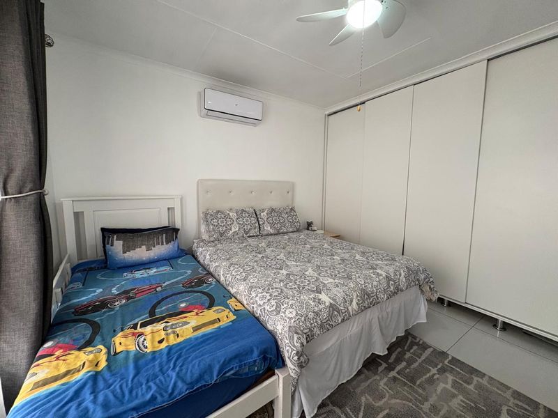 A well-maintained bedroom featuring built-in cupboards, a ceiling fan, and a wall-mounted split-system air conditioner with tiled flooring.