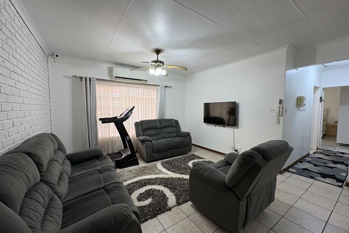 A comfortable living room featuring tiled flooring, an exposed brick feature wall, a ceiling fan, and a wall-mounted split-system air conditioner.