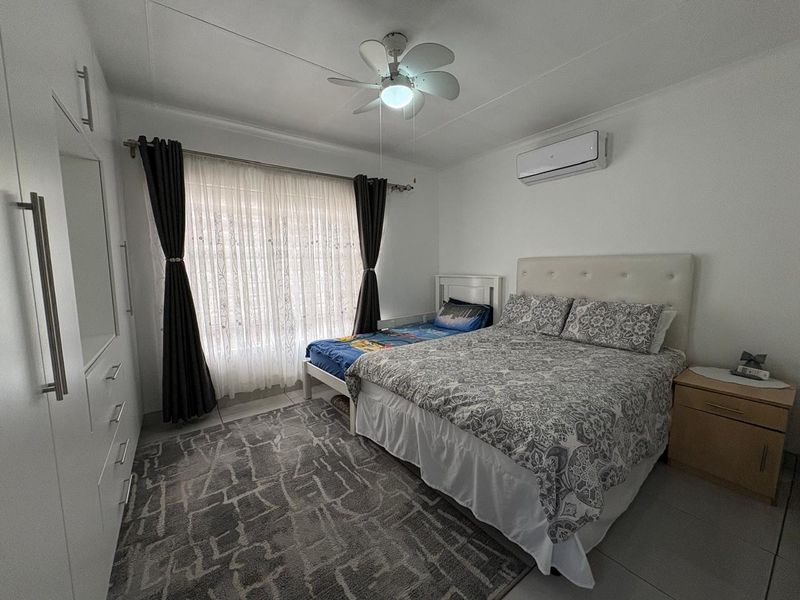 A well-maintained bedroom featuring a ceiling fan, split-system air conditioning, and built-in wardrobe storage with tiled flooring.