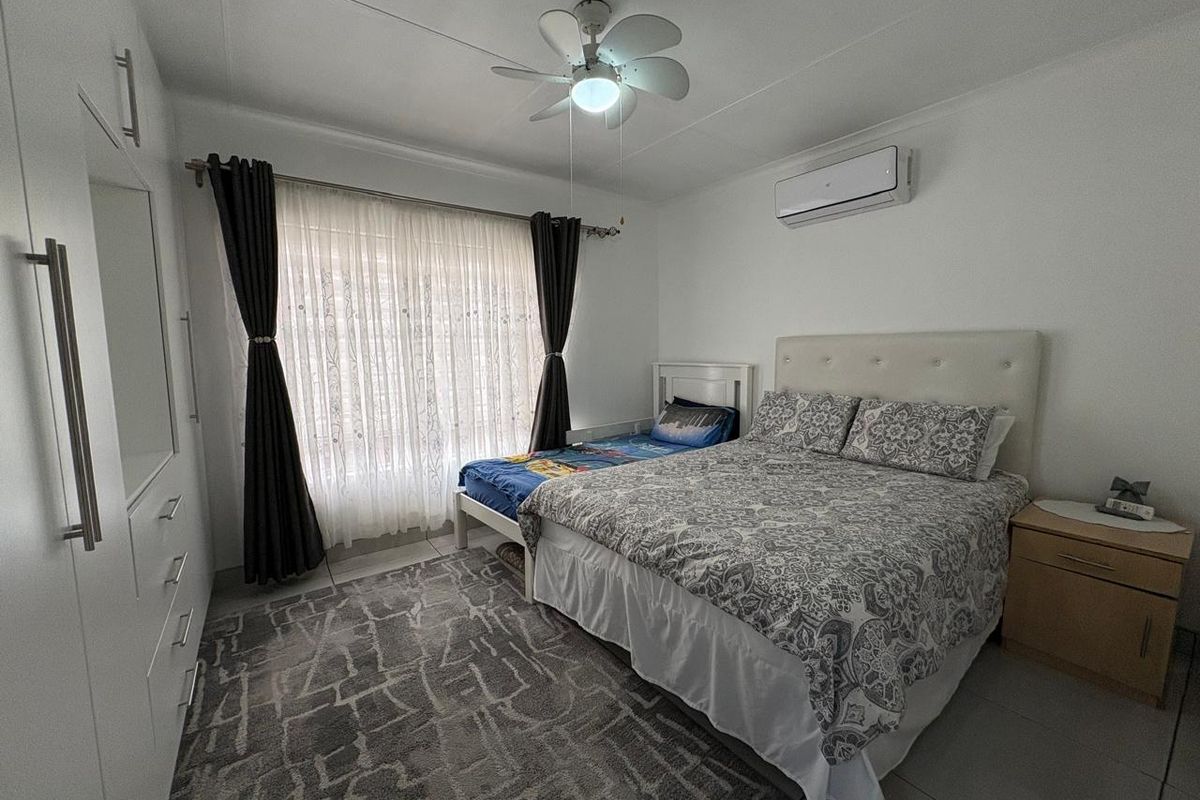 A well-maintained bedroom featuring a ceiling fan, split-system air conditioning, and built-in wardrobe storage with tiled flooring.