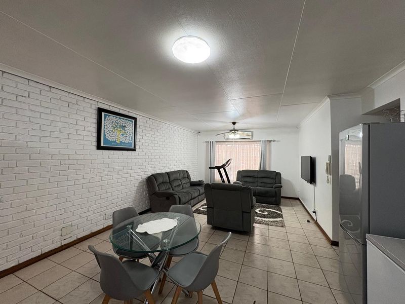 Spacious open-plan living and dining area featuring tiled flooring, a textured white brick feature wall, and a ceiling fan.
