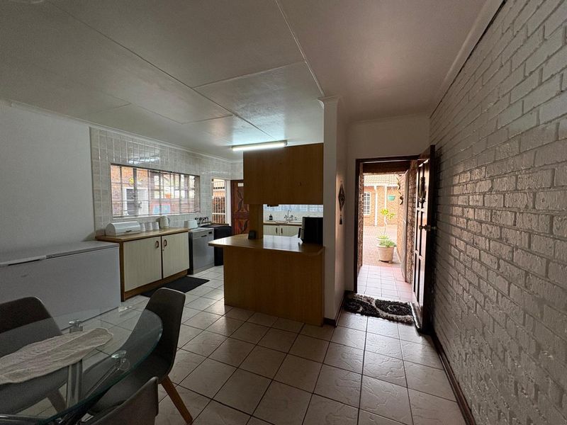 Open plan kitchen and dining area featuring tiled floors, built-in cabinetry, a breakfast bar, and an exposed brick wall with direct access to the rear courtyard.