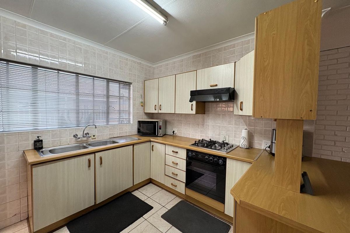 A functional kitchen featuring laminate cabinetry, a gas hob, built-in oven, extractor fan, and tiled backsplash with a double basin sink.