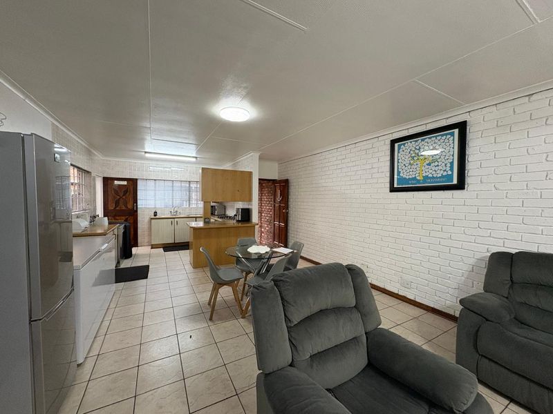 Open plan living and kitchen area featuring tiled flooring, painted brick walls, and functional kitchen cabinetry.