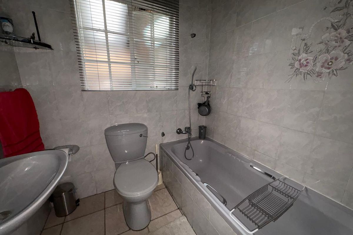 A functional bathroom featuring a bathtub, toilet, and pedestal basin with neutral wall and floor tiling.