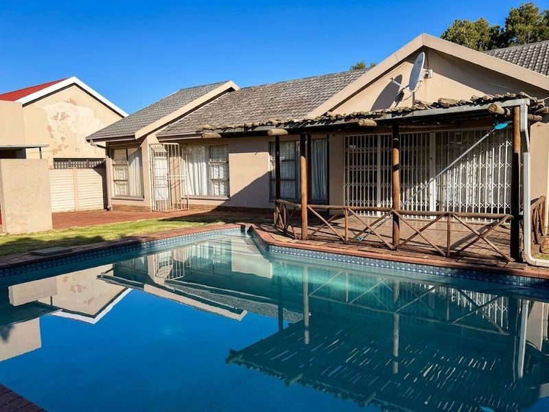 Rear exterior view featuring a swimming pool, wooden deck, and pergola, with access to the main house through security gates.