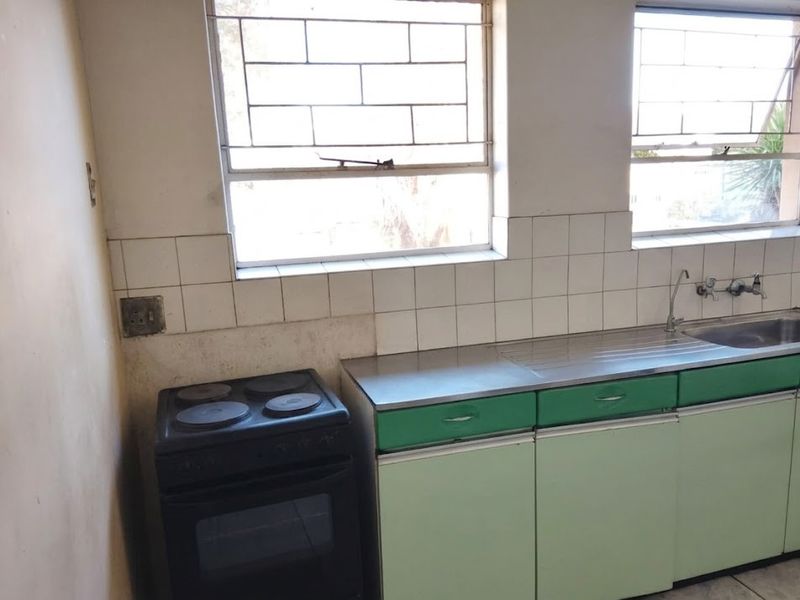A functional kitchen featuring built-in cabinetry, a stainless steel sink, and an electric stove, with tiled splashbacks and security-barred windows.