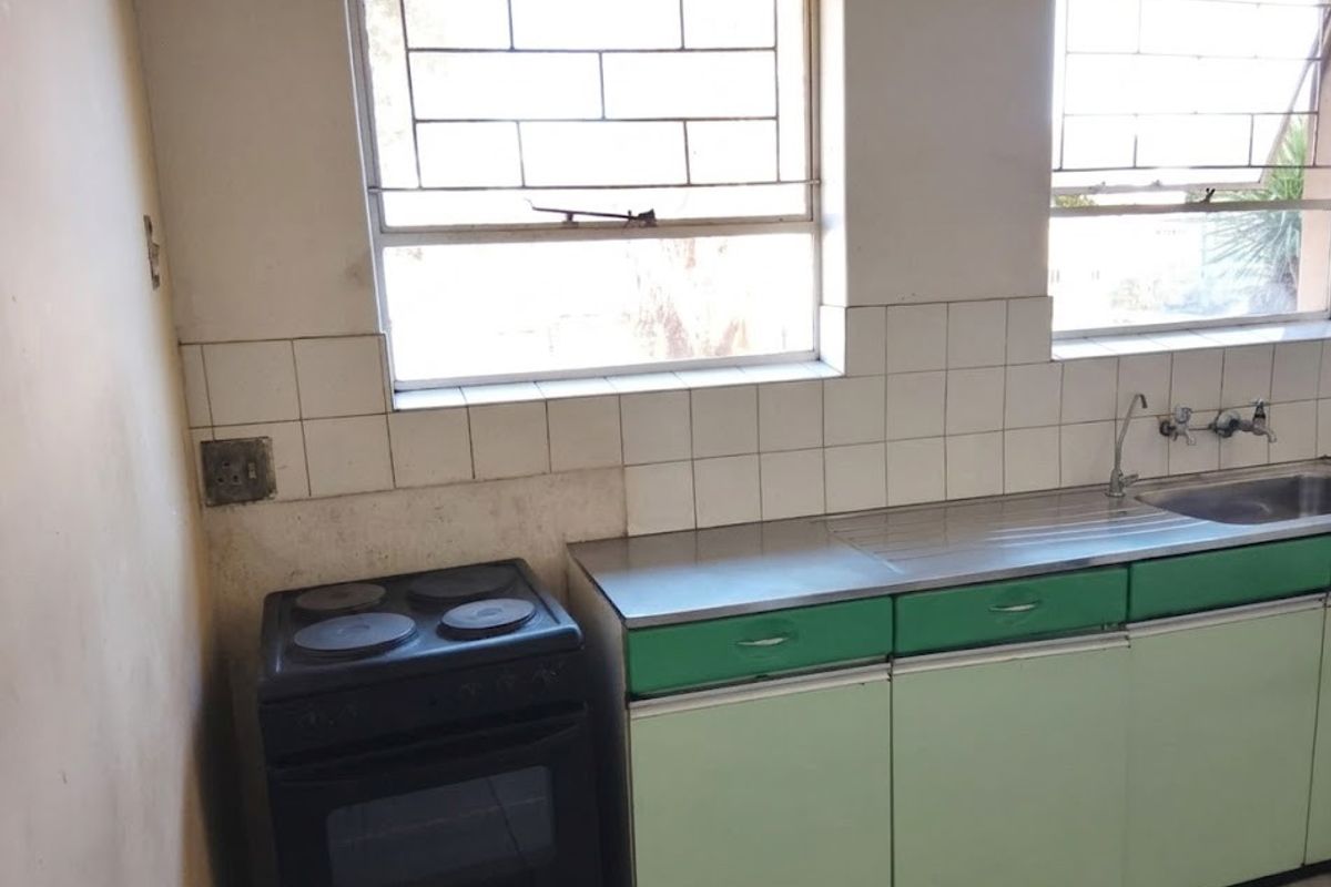 A functional kitchen featuring built-in cabinetry, a stainless steel sink, and an electric stove, with tiled splashbacks and security-barred windows.