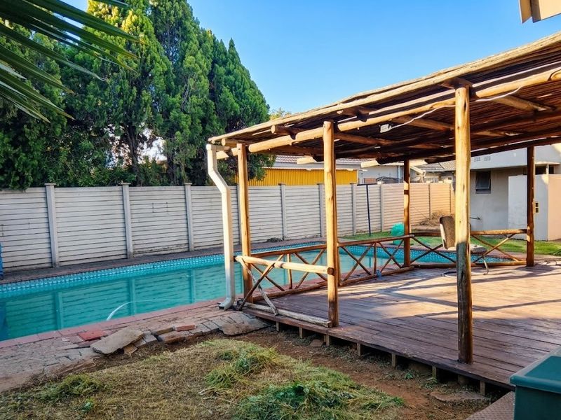 Outdoor pool area featuring a wooden deck with a timber pergola, adjacent to a swimming pool and enclosed by a precast boundary wall.
