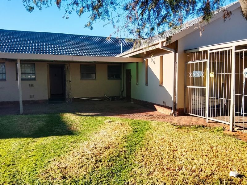 Rear view of the property featuring a covered patio area, brick paving, and a lawn with a tiled roof structure.