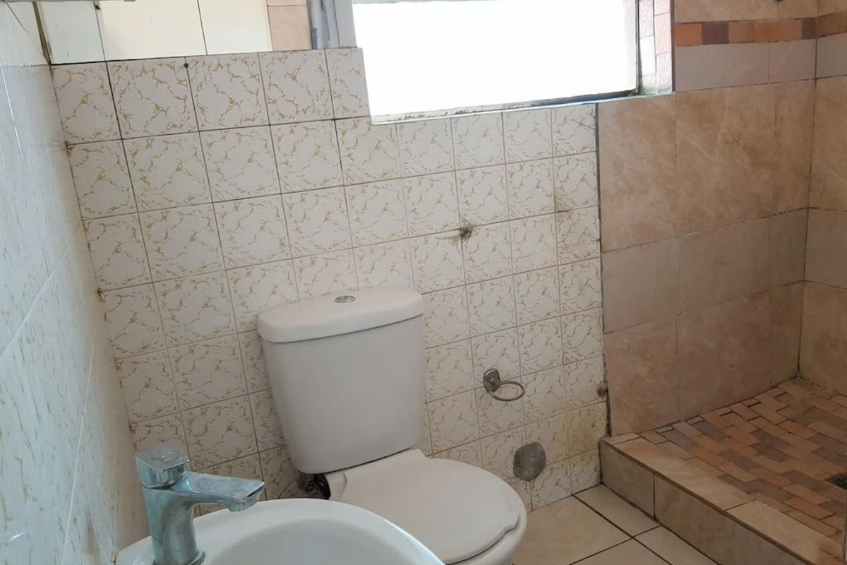 A dated bathroom featuring a toilet, washbasin, and shower area with tiled finishes, requiring cosmetic updates and maintenance to improve its overall condition.