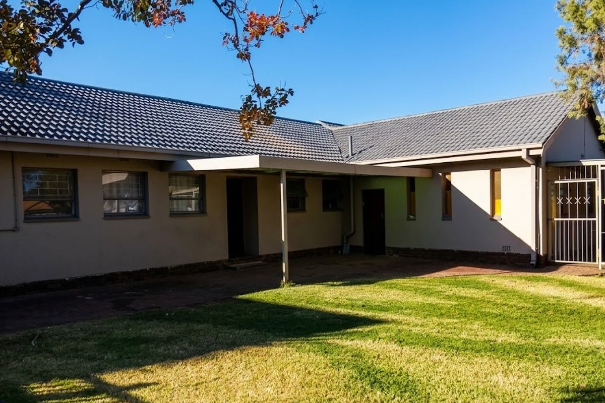 Rear view of the house featuring a tiled roof, a covered patio area, and a well-maintained lawn with paved pathways.