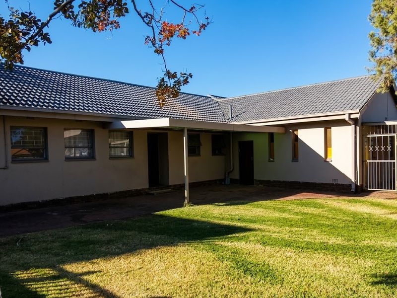 Rear view of the house featuring a tiled roof, a covered patio area, and a well-maintained lawn with paved pathways.