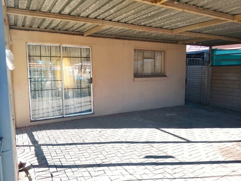 A covered outdoor patio area featuring paved flooring, a corrugated metal roof, and direct access to the home via a sliding glass door.