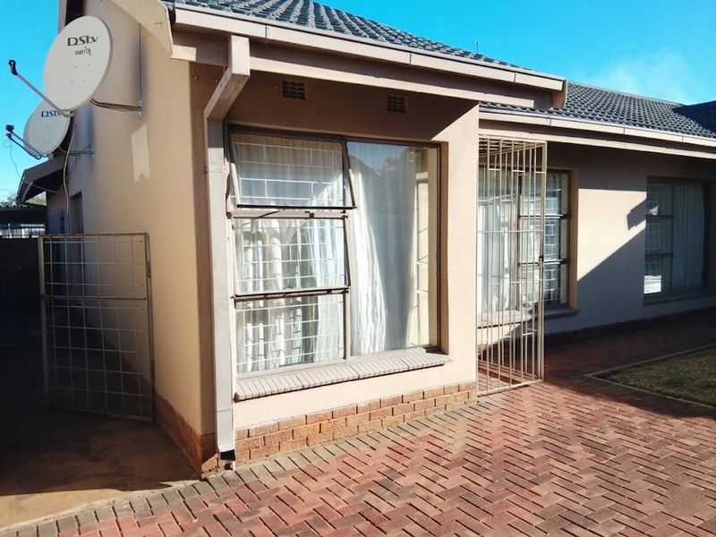 A view of the rear exterior of the house featuring brick paving, tiled roofing, and security bars on the windows.