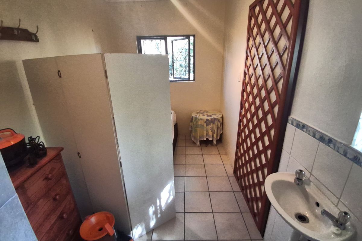A functional bedroom space featuring tiled flooring, a wall-mounted basin, and a window with security bars.