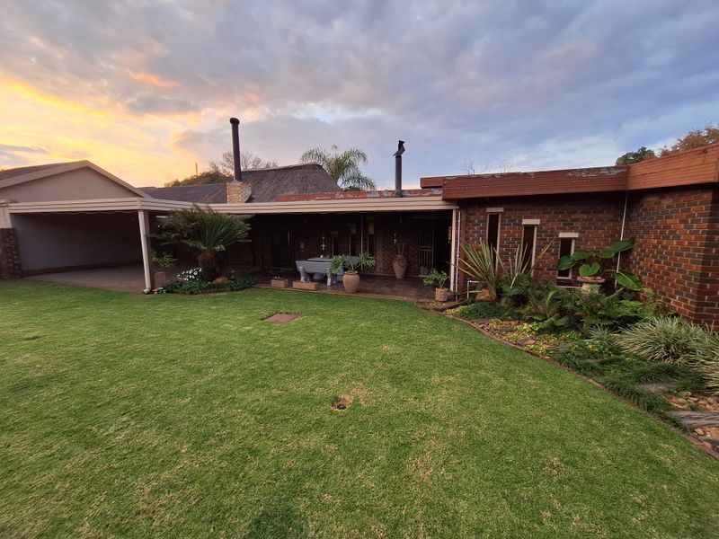 Rear view of the property featuring a covered patio area, brick facade, and a well-maintained lawn with established garden beds.