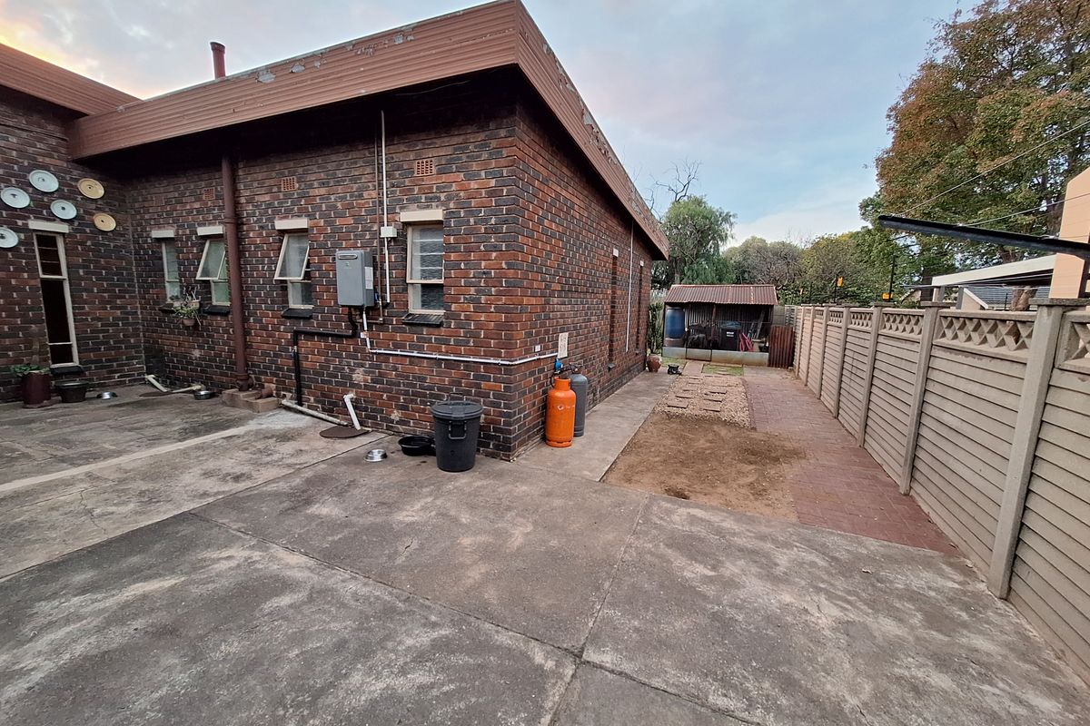 Rear exterior view of the property featuring face brick walls, concrete paving, a precast boundary wall, and a small garden shed.