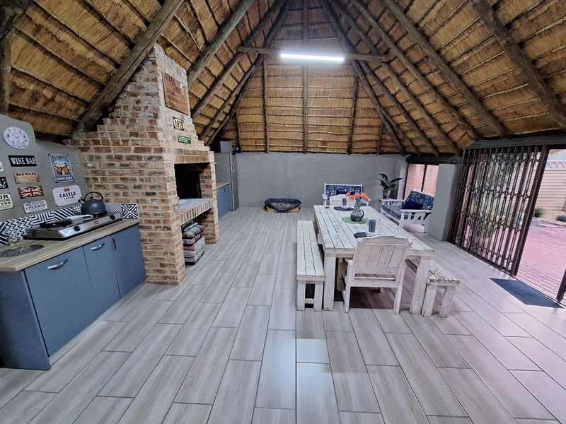 Spacious covered patio featuring a traditional thatched roof, exposed brick fireplace, built-in cabinetry, and modern tiled flooring, ideal for outdoor entertaining.