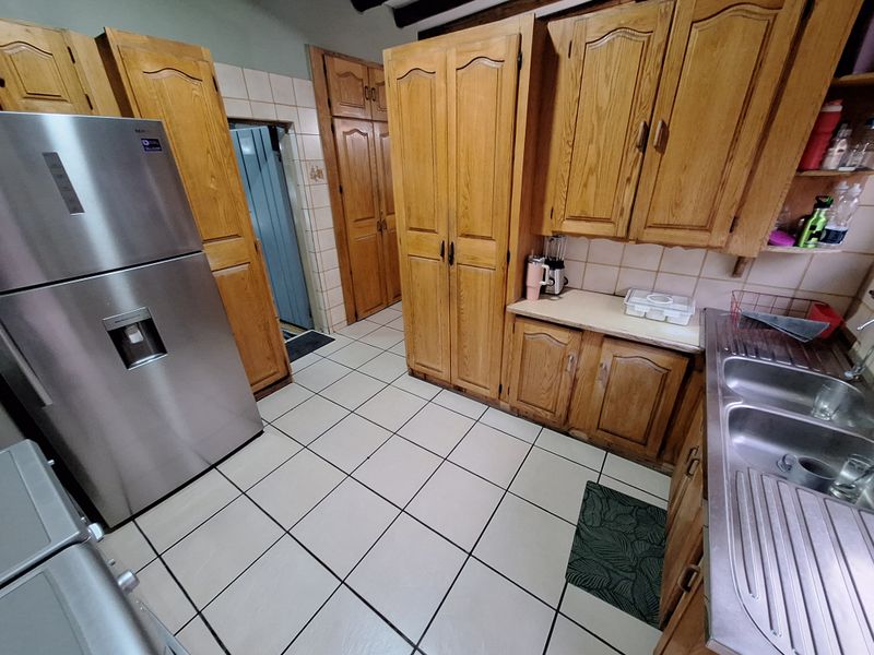A functional kitchen featuring traditional wooden cabinetry, tiled flooring, and a double stainless steel sink with ample built-in storage space.
