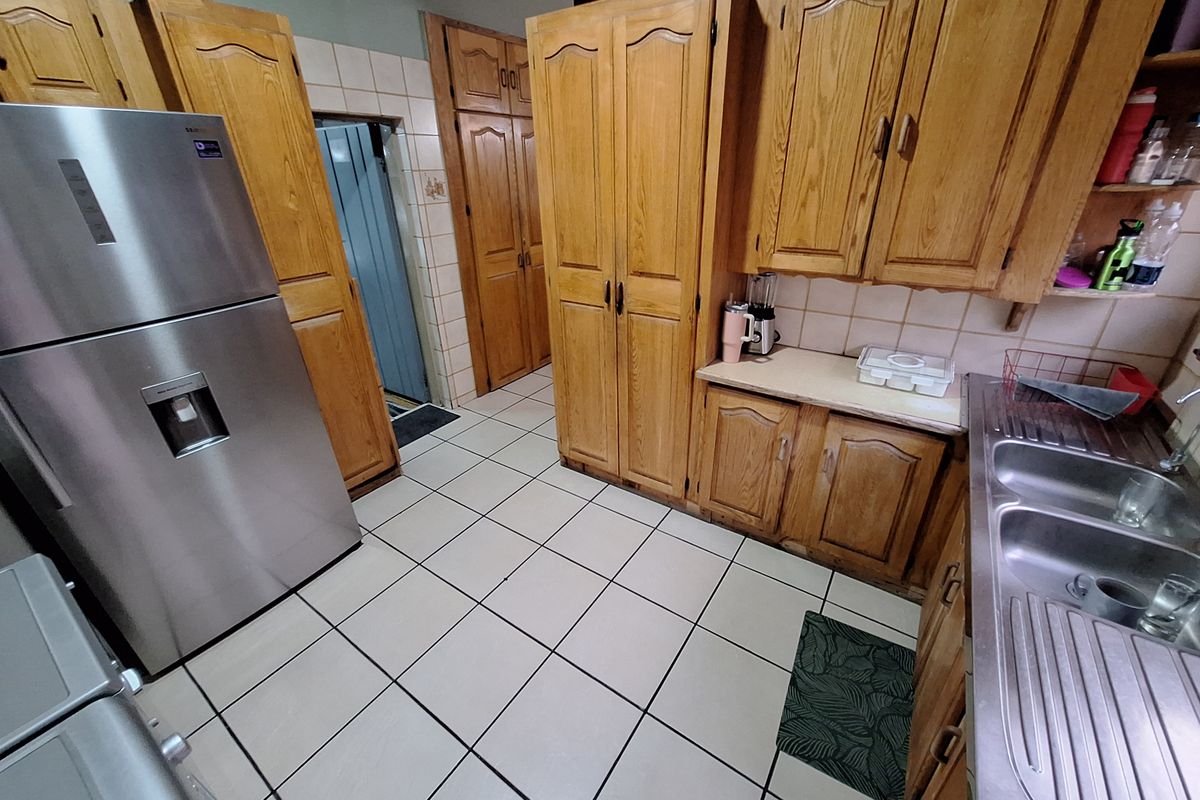 A functional kitchen featuring traditional wooden cabinetry, tiled flooring, and a double stainless steel sink with ample built-in storage space.