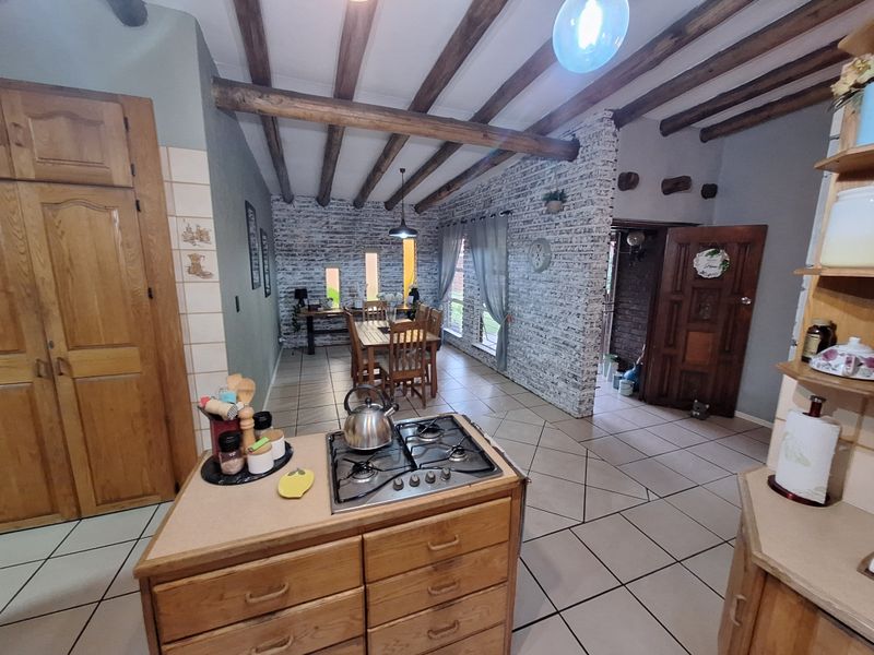 Open-plan kitchen and dining area featuring exposed timber ceiling beams, a rustic brick feature wall, and a central kitchen island with a gas cooktop.