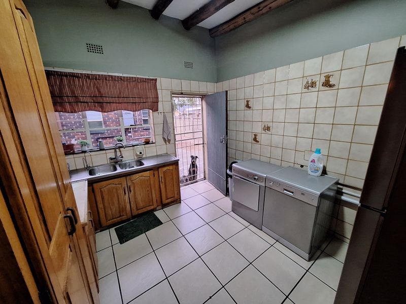 Functional laundry room featuring tiled flooring, built-in wooden cabinetry, double stainless steel sink, and exposed timber ceiling beams.