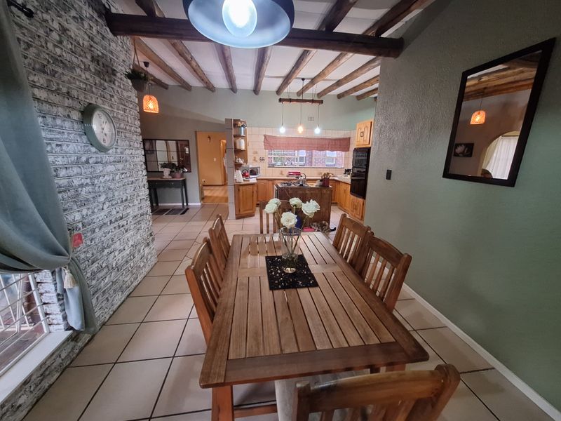 Open-plan dining and kitchen area featuring exposed timber ceiling beams, a rustic brick feature wall, and tiled flooring throughout.