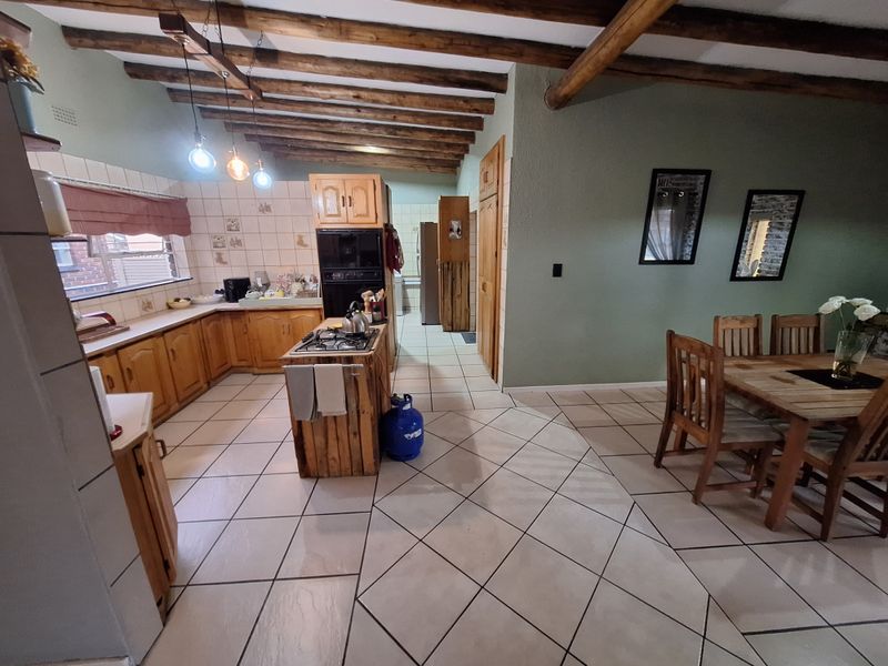 Open-plan kitchen and dining area featuring exposed timber ceiling beams, tiled flooring, and traditional wooden cabinetry with a central island hob.