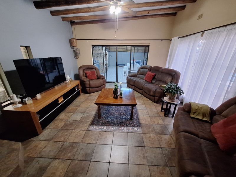Spacious living room featuring exposed timber ceiling beams, tiled flooring, and large sliding glass doors providing access to the outdoor patio area.