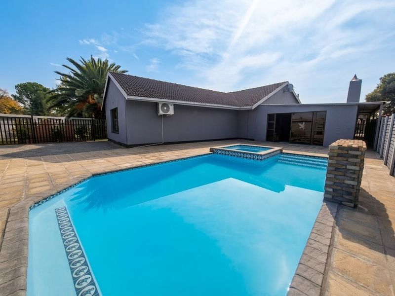 A well-maintained outdoor pool area featuring a swimming pool with an integrated spa, stone pillar detail, and paved surround.