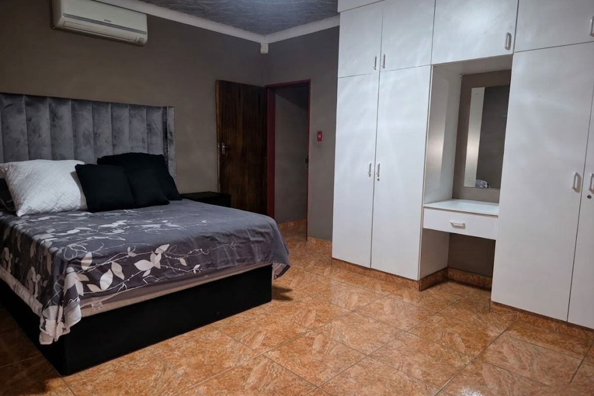 A bedroom featuring tiled flooring, a built-in wardrobe with an integrated vanity, and a wall-mounted air conditioning unit.