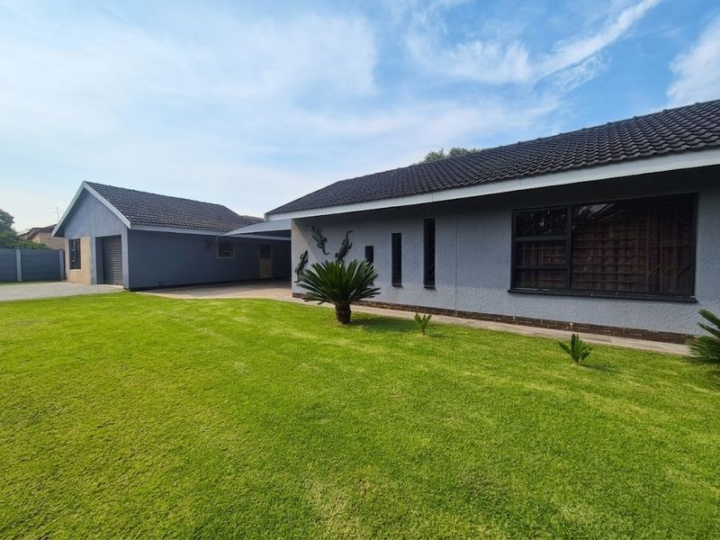 A well-maintained single-story house featuring a grey rendered facade, tiled roof, paved driveway, and an attached garage with a carport.