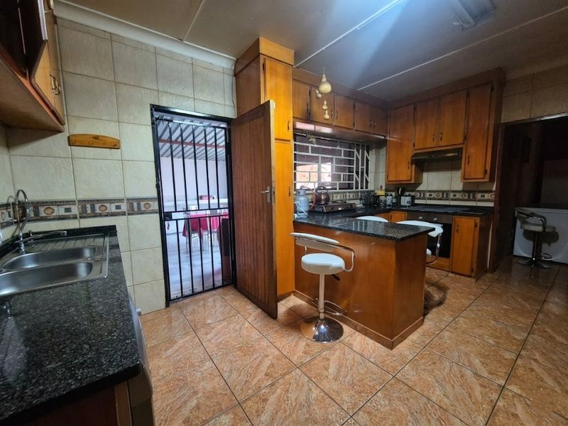 A functional kitchen featuring wooden cabinetry, granite countertops, a double basin sink, and built-in cooking appliances with direct access to an outdoor area.