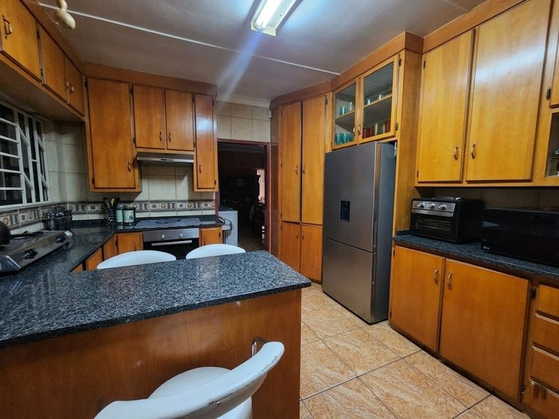 A functional kitchen featuring extensive wooden cabinetry, granite countertops, a breakfast bar, and tiled flooring, offering a classic layout with ample storage space.