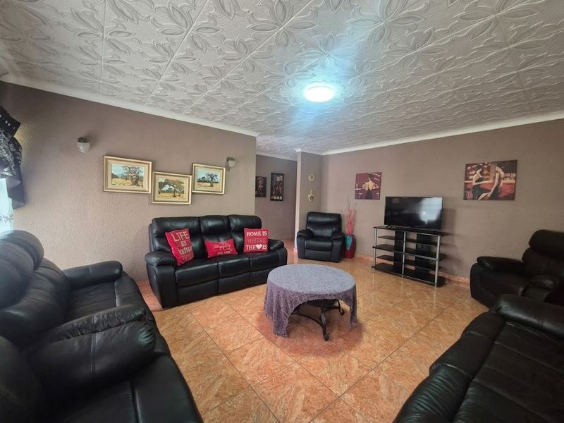 A spacious living room featuring patterned ceiling tiles, ceramic floor tiling, and wall-mounted lighting fixtures.