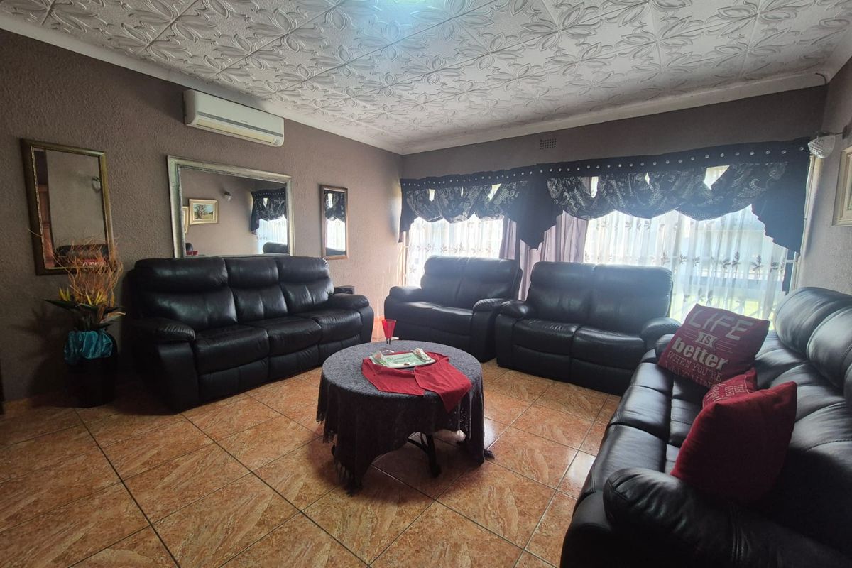A living room featuring tiled flooring, decorative ceiling tiles, and a wall-mounted air conditioning unit.