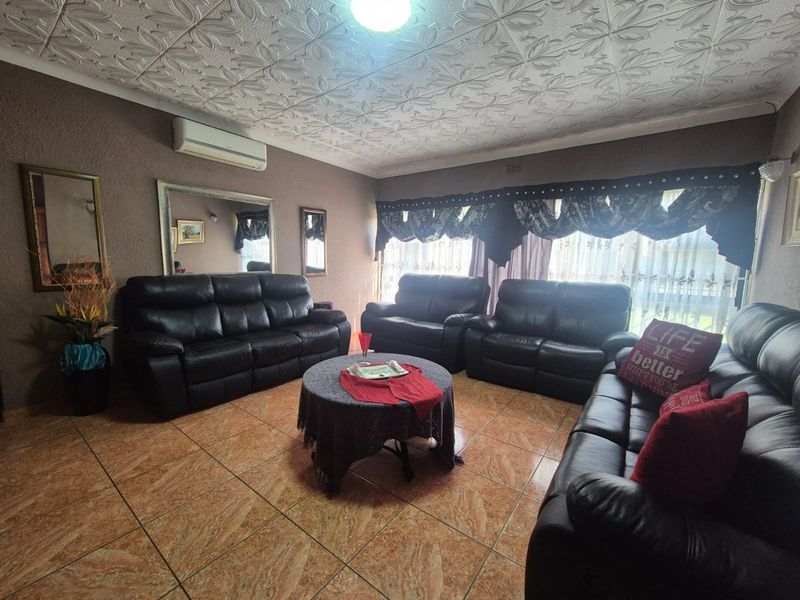 A living room featuring tiled flooring, decorative ceiling tiles, and a wall-mounted air conditioning unit.