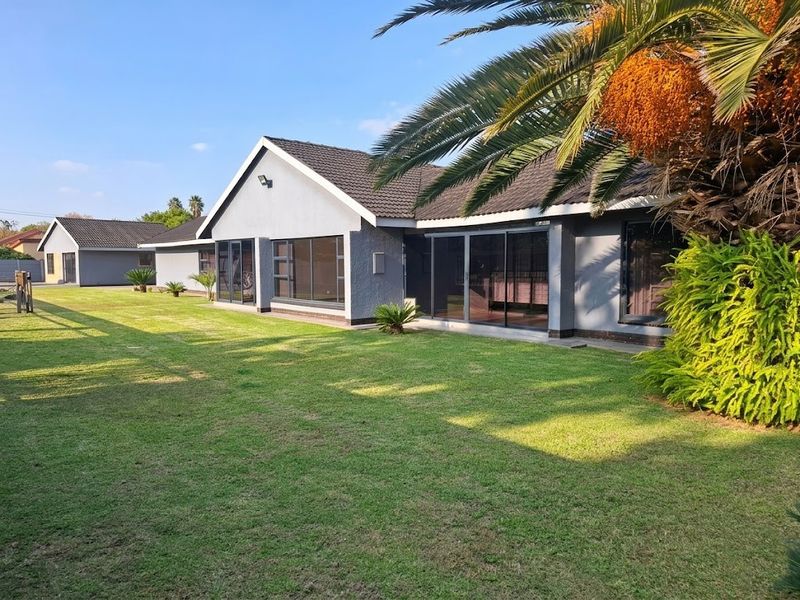 A well-maintained rear exterior view of the house featuring a spacious lawn, tiled roof, and large sliding glass doors providing access to the interior.