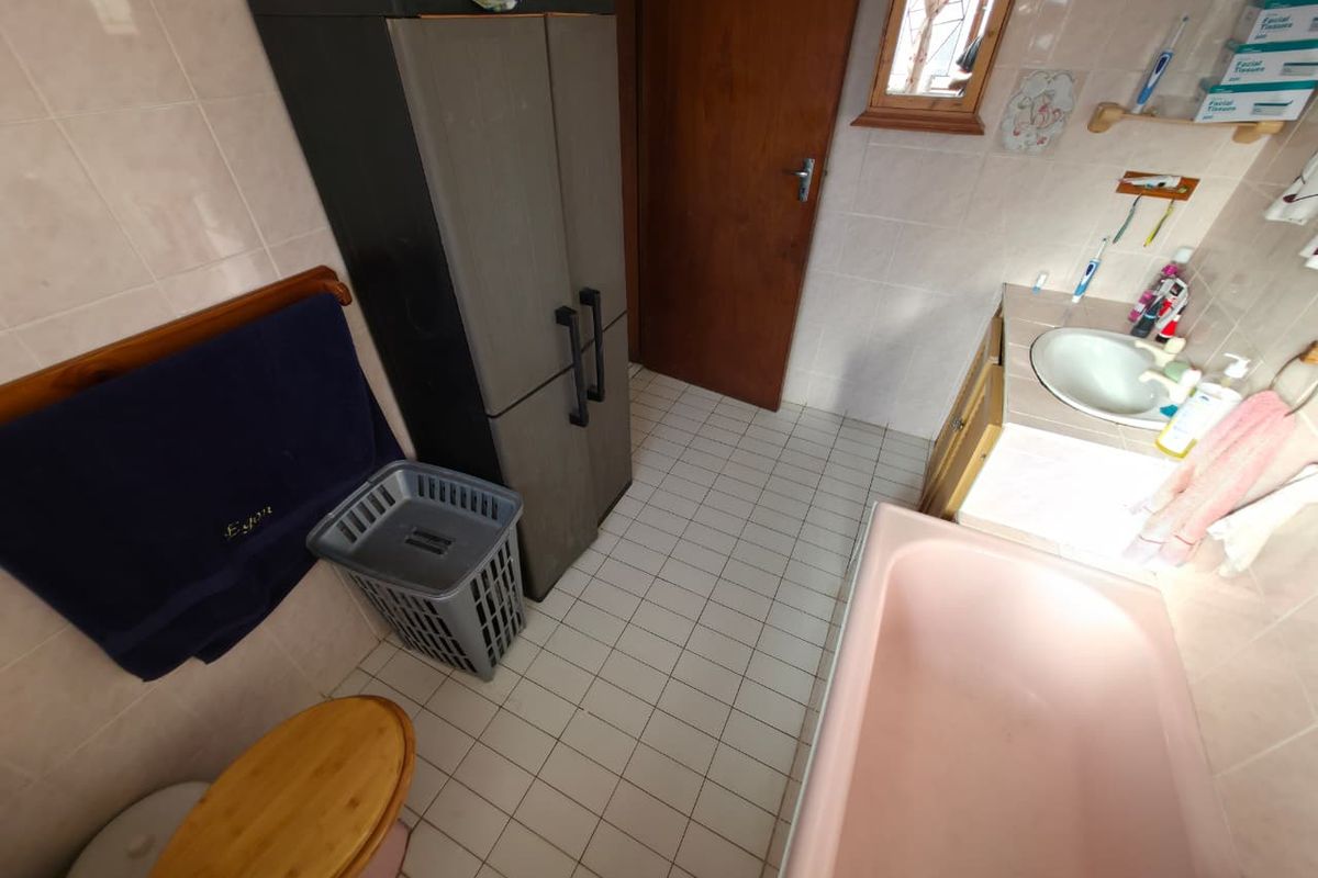 A functional bathroom featuring a pink bathtub, tiled walls and flooring, and a built-in vanity unit with a ceramic basin.