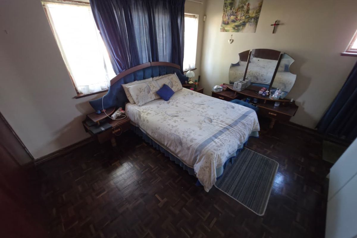 A bedroom featuring dark parquet flooring and natural light from large windows.