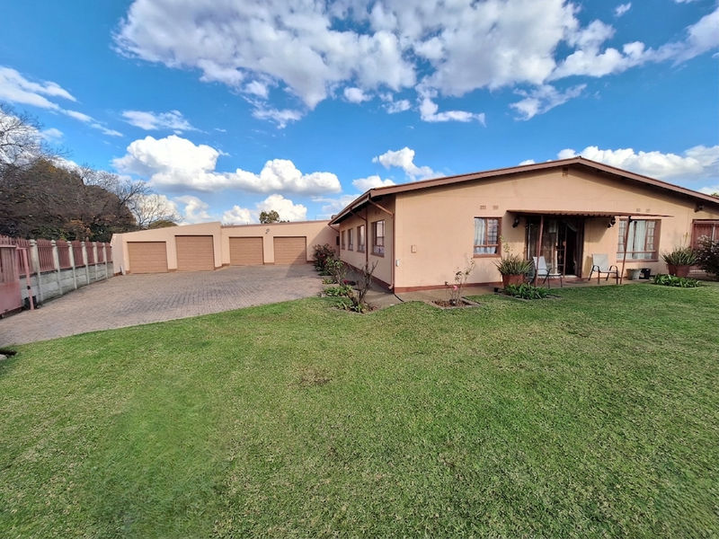 Rear view of the property featuring a large lawn, paved driveway, multiple garage doors, and a covered patio area.