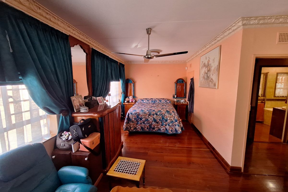 Spacious bedroom featuring hardwood flooring, crown molding, a ceiling fan, and built-in vanity mirrors, with an adjoining bathroom visible through the doorway.