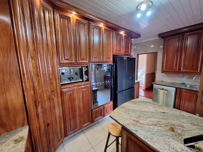 A well-appointed kitchen featuring rich wood cabinetry, granite countertops, integrated appliances, and a classic tongue and groove ceiling finish.