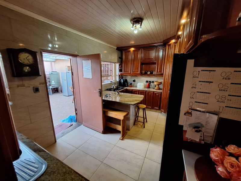 A functional kitchen featuring warm wooden cabinetry, granite countertops, tiled flooring, and a tongue and groove ceiling, with direct access to an outdoor area.