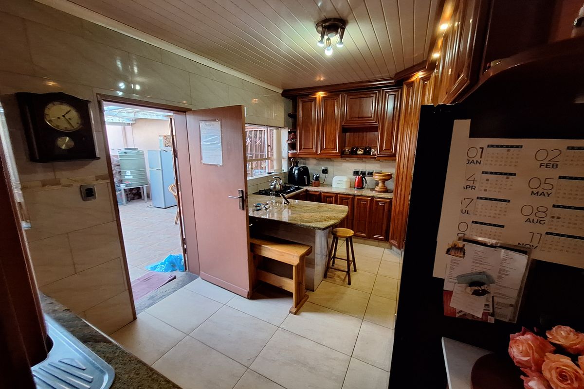 A functional kitchen featuring warm wooden cabinetry, granite countertops, tiled flooring, and a tongue and groove ceiling, with direct access to an outdoor area.
