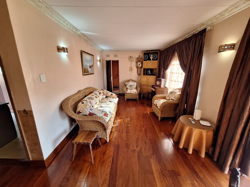 A living room featuring polished hardwood flooring, decorative ceiling cornices, and wall-mounted lighting, offering a warm and traditional aesthetic.